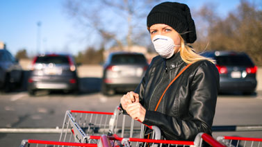 Woman wearing a medical mask while pushing a cart in a parking lot