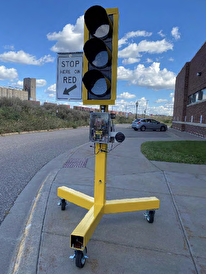 A prototype traffic signal mounted on a stand with rollers sits at a roadside