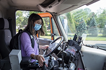 White teenage girl with brown hair and glasses in driver's seat of a plow truck
