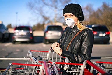 Blond woman wearing a hat, coat, and N95 mask with shopping carts outside