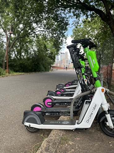 A row of Lime scooters parked by the side of a paved trail