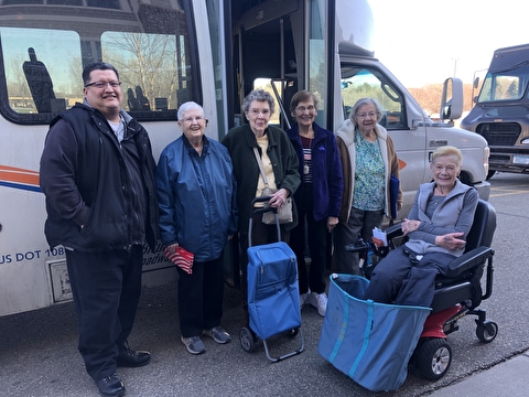 Older adults, including one in a wheelchair, outside a transit bus