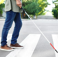 Visually impaired pedestrian using a white can to cross a street at a marked crosswalk