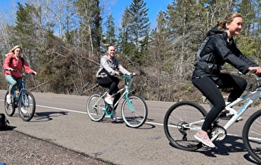 Three people riding bikes on a road shoulder