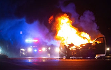 Crashed vehicle on fire with a police car in the background