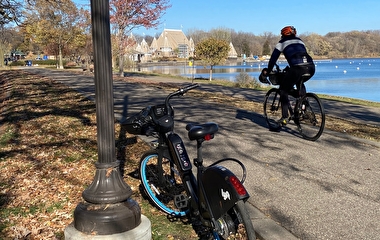 Bicyclist riding on a paved trail by a lake in the autumn