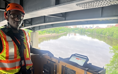 MnDOT intern Ryan Mwangi used a snooper to inspect a bridge high above the Mississippi River.