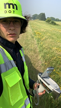 Intern wearning a safety vest in the field, holding a scanning gun for testing bridges