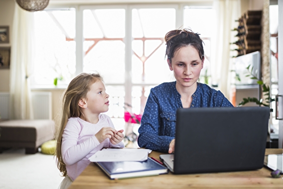 Young girl looking at her mother, who is working on a laptop