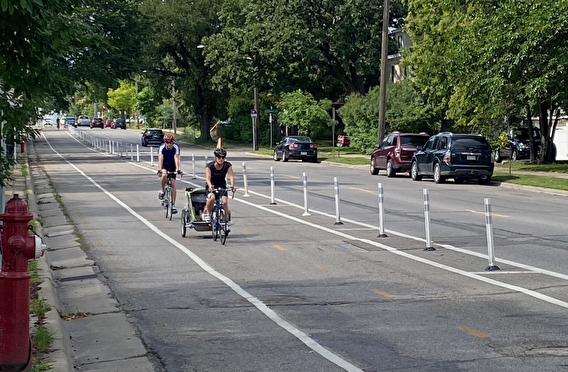Two people riding bikes in a bike lane separated by bollards