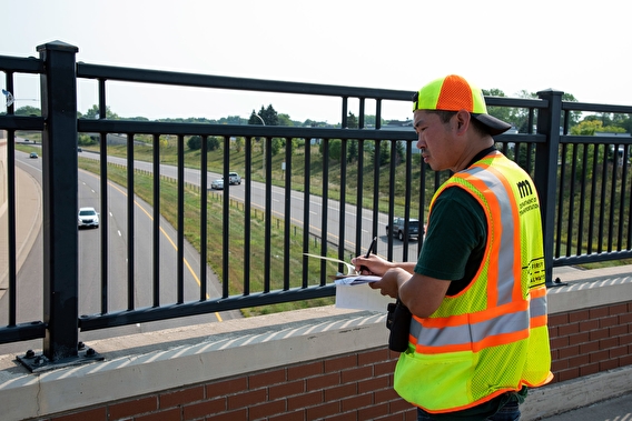 MnDOT intern Charles Sisterman writing on a clipboard while standing on an overpass