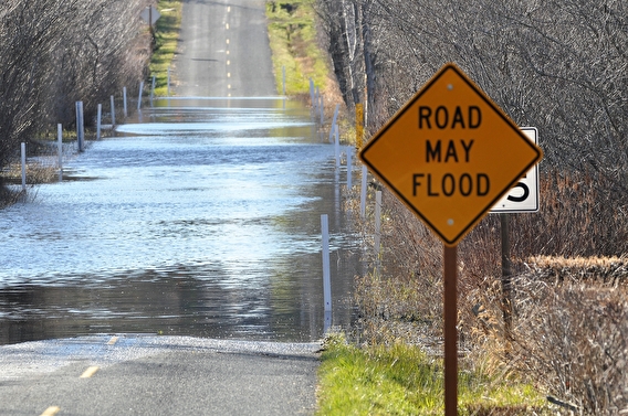A sign saying "Road may flood" with a flooded roadway in the background