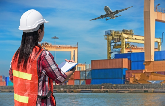 Woman holding a clipboard working in a shipyard with a jet flying overhead