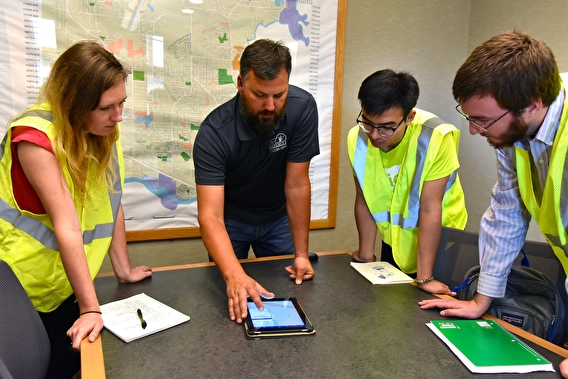 Four people in reflective vests gathered around a desk with a tablet