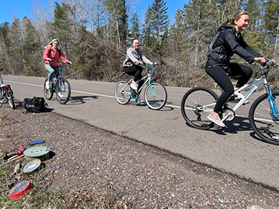Three people riding bikes on a paved road shoulder