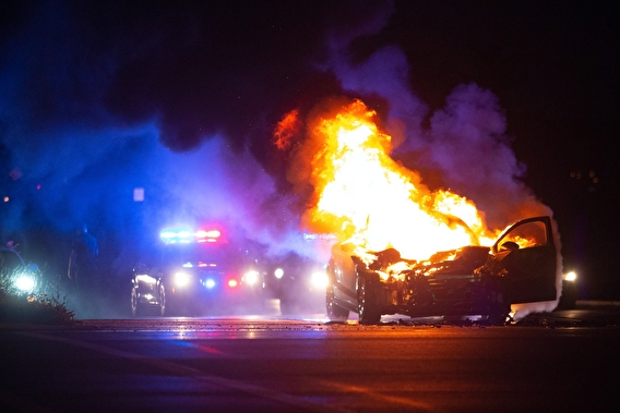 Crashed vehicle on fire with a police car in the background