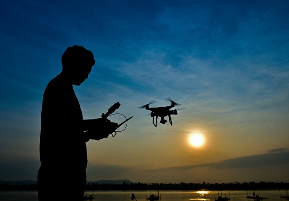 Silhoutted drone operator and flying drone in front of a sunset