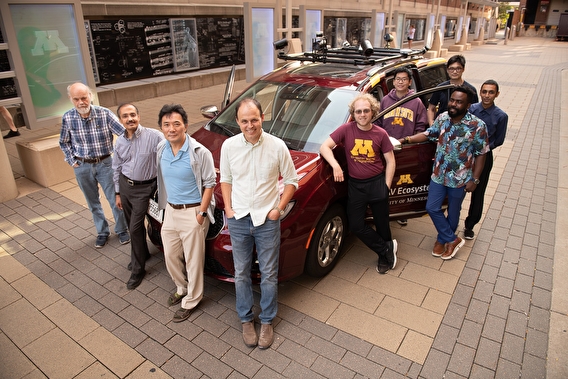 The project team standing around the maroon Chrysler Pacifica automated vehicle