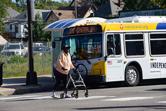 Woman using a walker as she crosses a crosswalk with a bus in the background