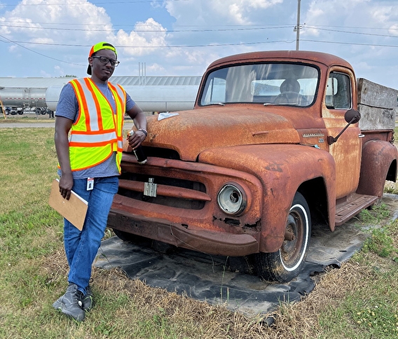 MnDOT intern Ryan Mwangi leaning against an old trucck wearing a safety vest 