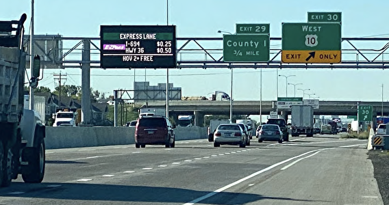 Vehicles on a freeway with a managed lane electronic sign displaying dynamic prices overhead