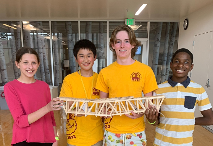 Four students pose with their popsicle stick bridge
