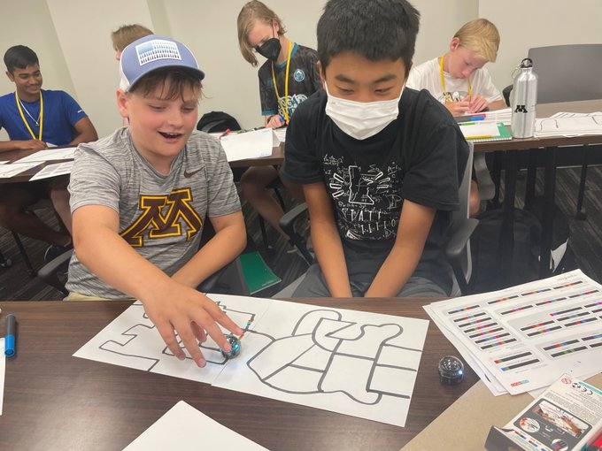 Two students sitting at a desk with an Ozobot