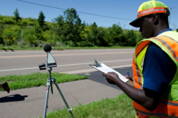 MnDOT intern with noise monitoring equipment at a roadside