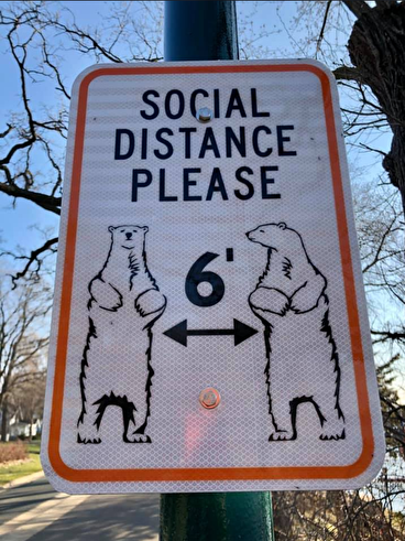 Trailside sign with cartoon bears that reads "social distance please" 