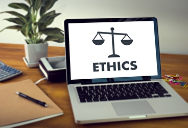 A laptop on a desk with the word "ethics" on the screen