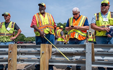 Four men in safety vests inspecting a section of guardail
