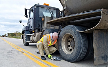 A man in a safety vest placing a scale beneath the tire of a semi trcuk
