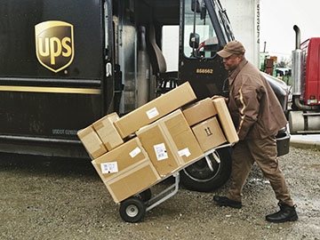 UPS driver with cart of packages next to delivery vehicle