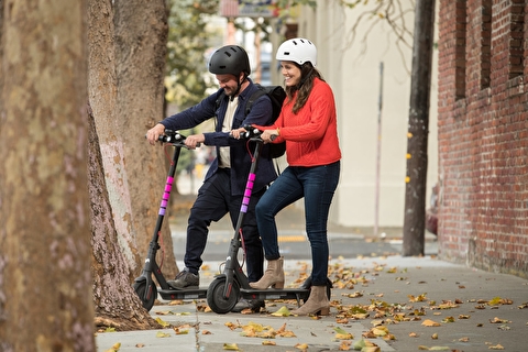 Two people standing on city sidewalk with scooters