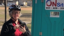 Woman wearing a bicycle helmet standing outside portable toilet