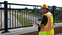 Intern writing on a clipboard while looking down at a road from an overpass